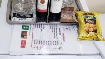 A minibar with two bottles of wine, several glasses, a packet of snacks, and a menu.