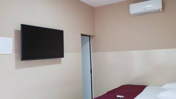 A hotel room with a bed, a TV mounted on the wall, a door, and an air conditioner.