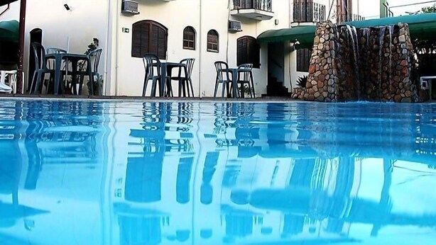 A swimming pool with clear water reflecting the surroundings. There are lounge chairs and tables around the pool area. - Hotel Malbec (Aparecida)