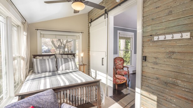A bedroom with a bed, a chair, a ceiling fan, and a wooden wall. - In-Town Saugatuck  “Magical Backyard” with Fire Pit Walk to Town (Saugatuck)