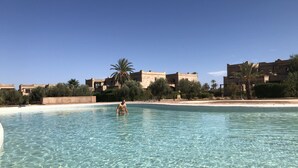 A clear pool with a person standing in the water, surrounded by buildings and palm trees. - Villa Mayrit. Beautiful Riyadh style villa in privileged surroundings (Marrakech)