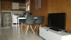 A modern kitchen with wooden accents, a dining area with two chairs, and a flat-screen TV on a white cabinet.