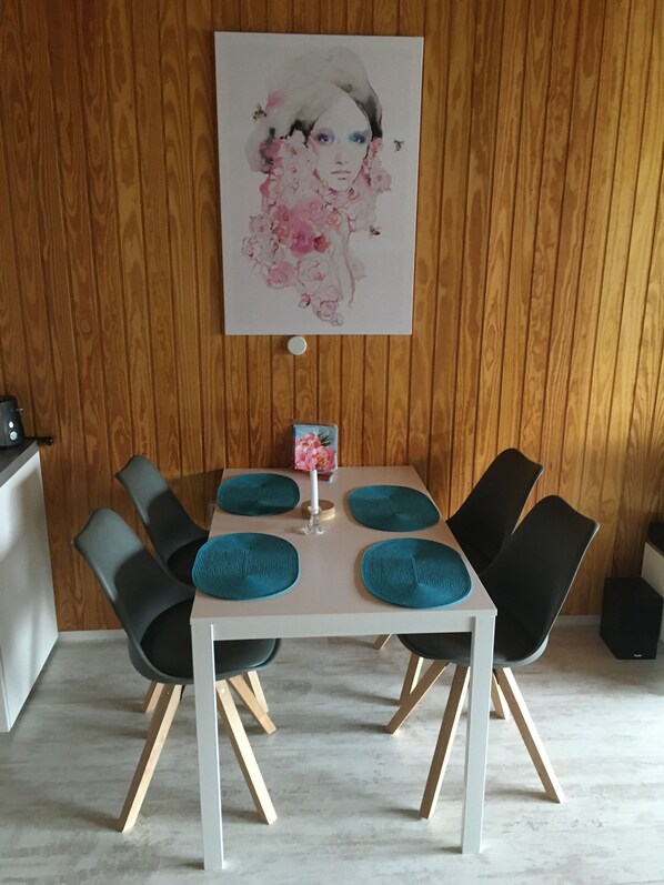 A dining area with a white table, four black chairs, teal placemats, and a framed artwork on the wall. - Apartment, centerpiece 'in the middle of the southern Black Forest (Todtnauberg)