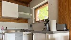 A compact kitchen with white cabinets, a window with a view, and a countertop with a kettle and a roll of paper towels.