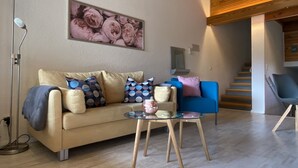 A living room with a beige sofa, a glass coffee table, and a blue armchair. A large floral painting adorns the wall above the sofa.