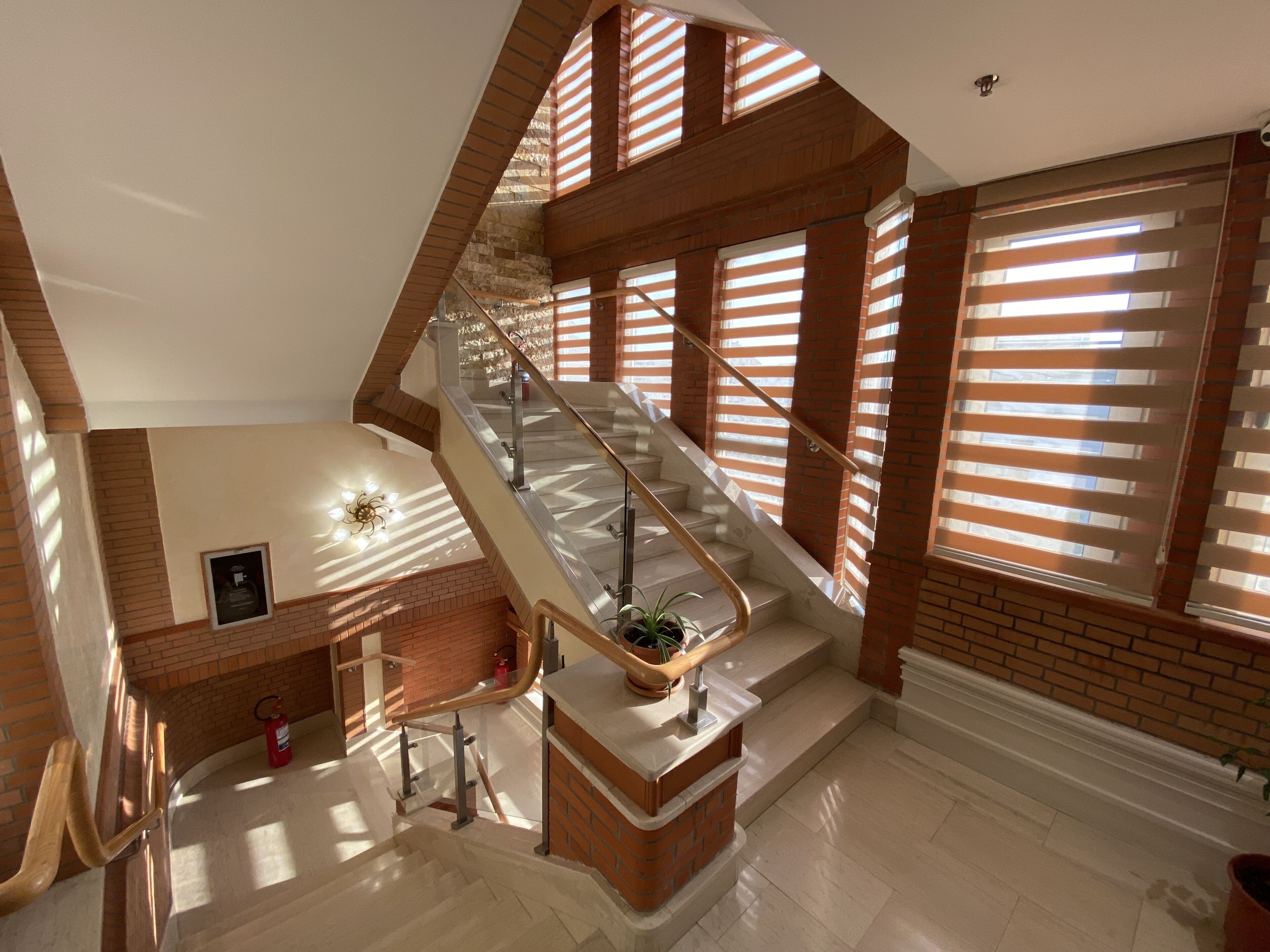 Un intérieur spacieux avec un escalier central, de grandes fenêtres équipées de stores et un extincteur posé sur le sol.