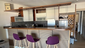 A modern kitchen with a central island, bar stools, and a striped backsplash.