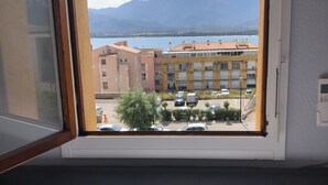 A hotel room with a window view of a building, a parking lot, and mountains in the distance.