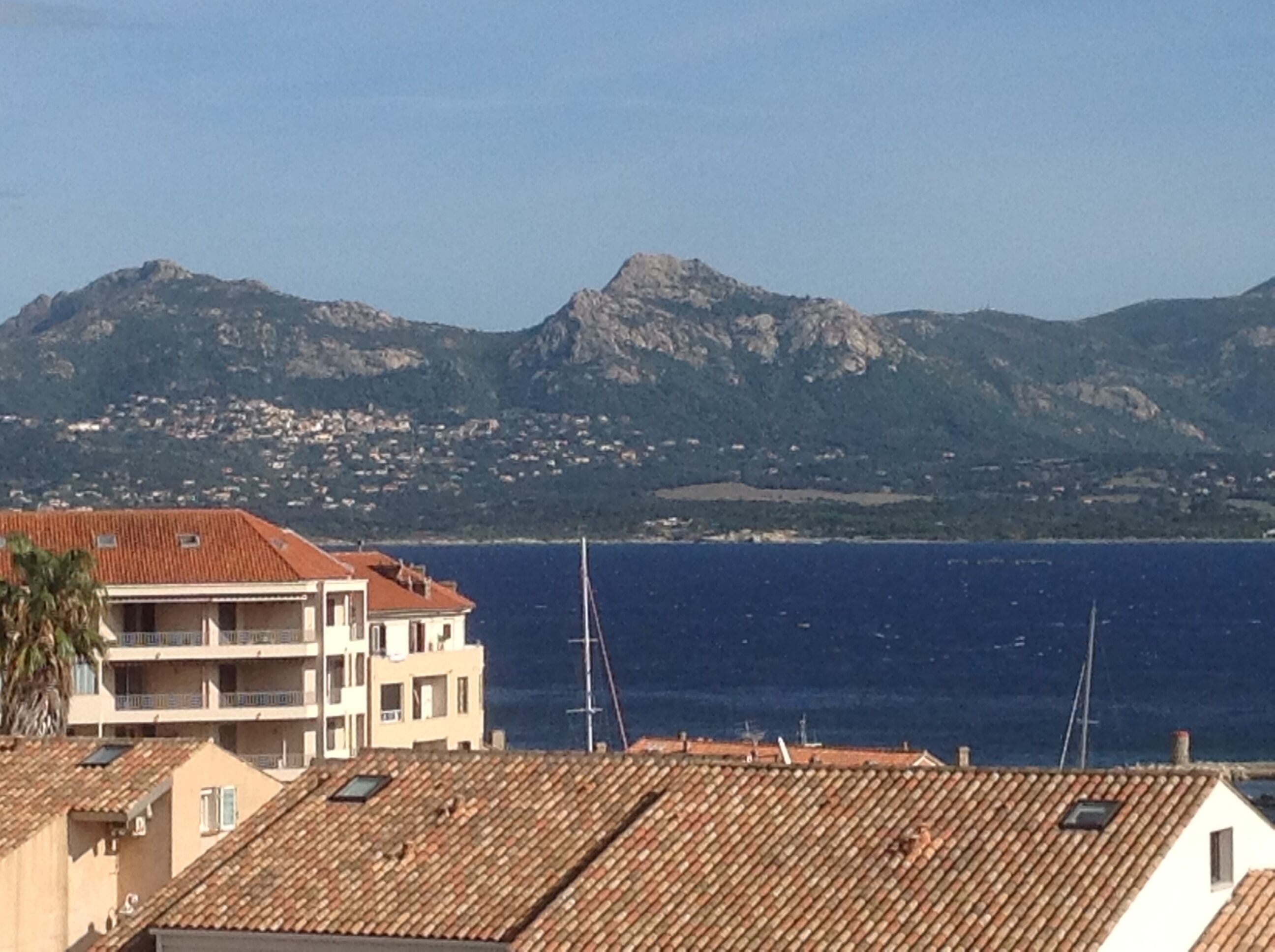 Un bâtiment situé sur la côte, doté d’un toit en tuiles, d’un balcon et offrant une vue sur la mer et les montagnes en arrière-plan.