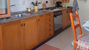 Una cocina con armarios de madera, encimera de granito, estufa y zona de comedor con una silla y mesa.