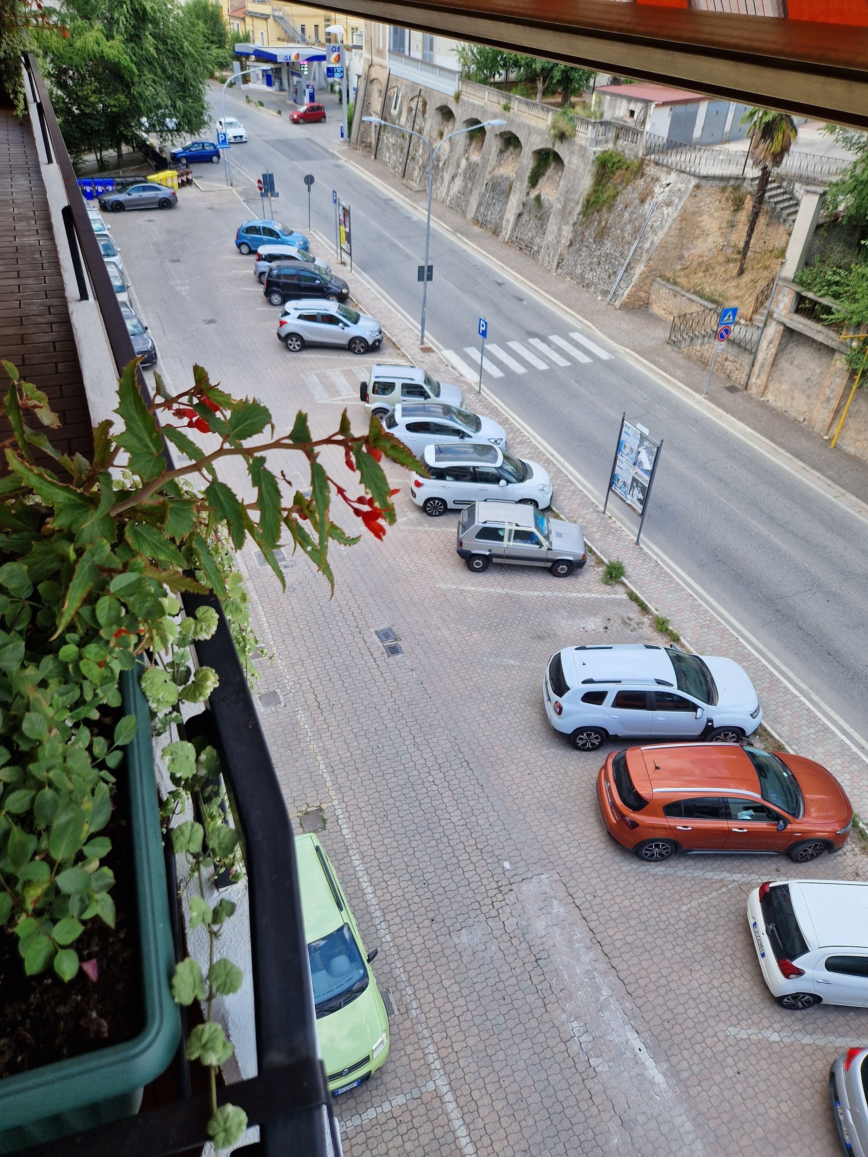 Une vue de rue avec des voitures garées, un passage piéton et un bâtiment à la façade en pierre.
