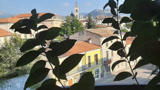 Vista de un paisaje urbano con edificios, una torre de iglesia y montañas al fondo.
