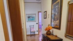 Un pasillo con piso de madera, una silla, una consola con un florero y obras de arte enmarcadas en las paredes.