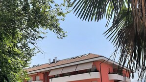 Un edificio de varios pisos con balcones, un estacionamiento con coches y un cielo despejado.