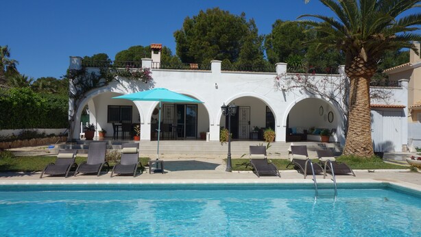 A poolside area with lounge chairs, a covered seating area, and a building with arches and a palm tree. - villa with private pool, 11 people, air conditioning located 200m from the beach (L' Ametlla de Mar)