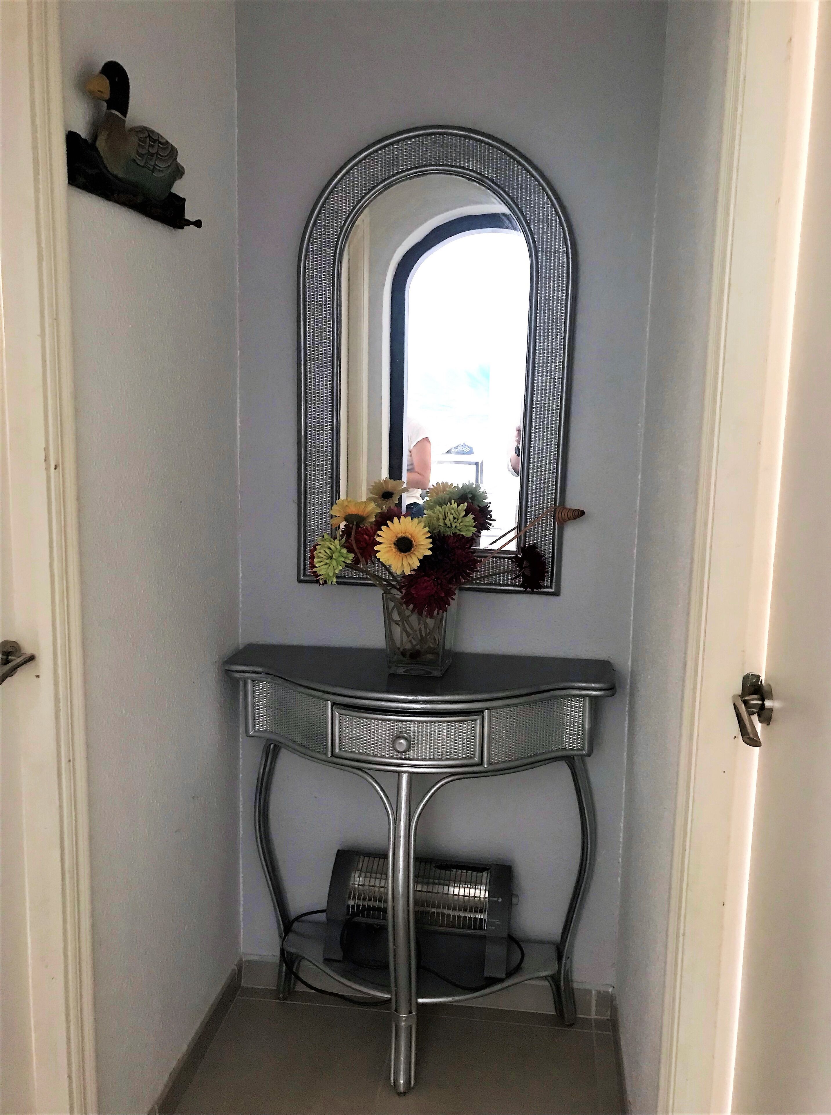 Un tocador de baño con espejo, un florero con flores y un calentador.