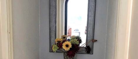 Un tocador de baño con espejo, un florero con flores y un calentador.
