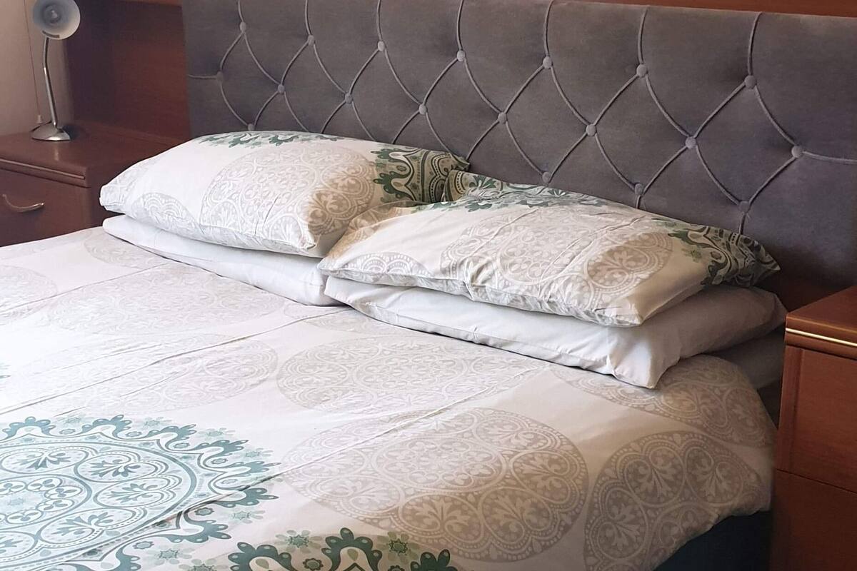 A neatly made bed with a patterned bedspread and two pillows, a wooden headboard, and a bedside table with a lamp.