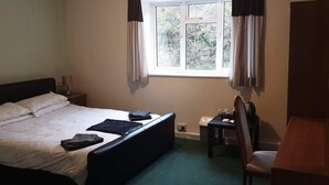 A bedroom with a bed, a nightstand, a desk, a chair, a window with curtains, and a radiator. - The Huntsman Hotel (Chepstow)