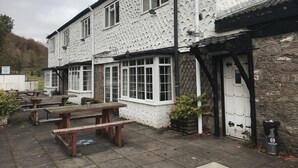 A building with a white exterior and multiple windows, featuring a stone wall and wooden beams. - The Huntsman Hotel (Chepstow)