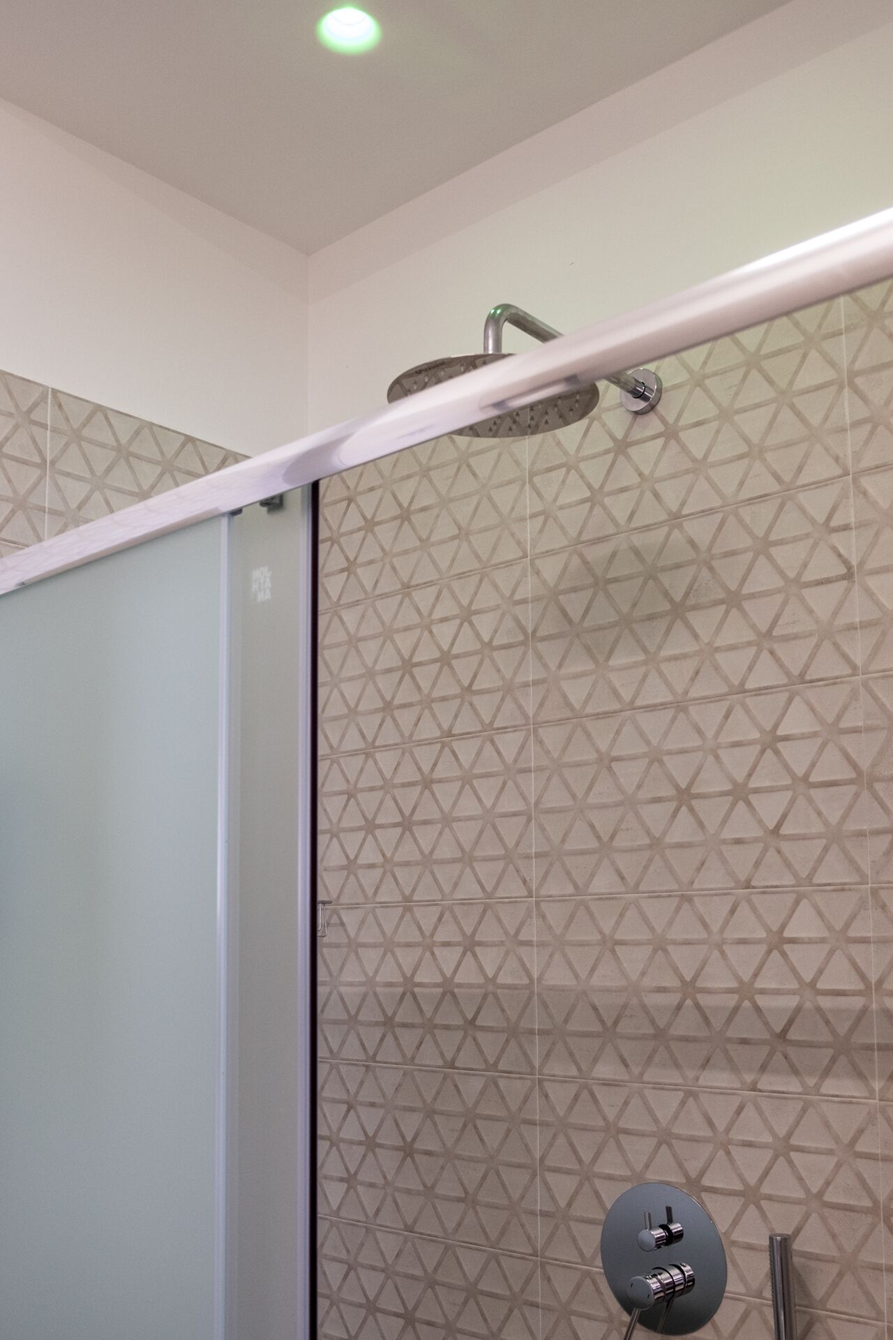 A shower with a modern design, a glass door, and a geometric patterned wall.