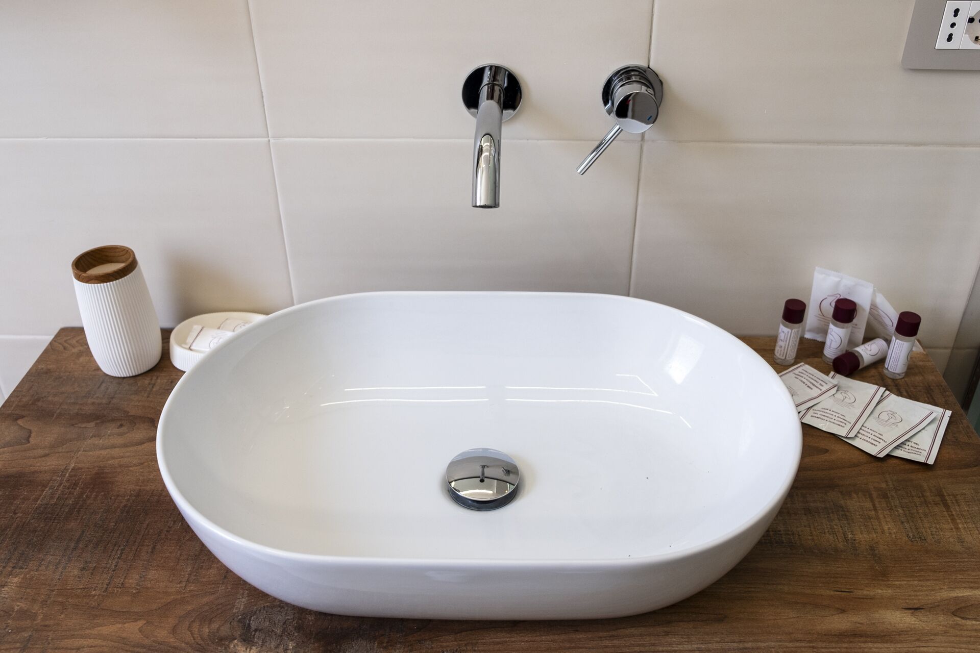 A bathroom with a white sink, two faucets, a wooden tray, a soap dish, and toiletries on the counter.