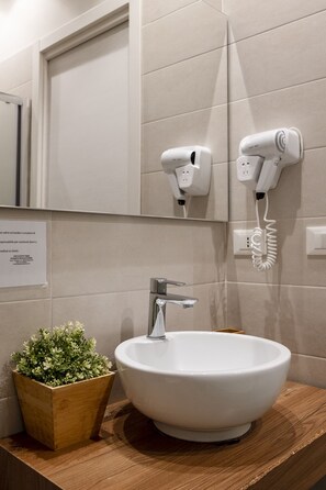 Une salle de bain avec un lavabo blanc, un miroir et deux sèche-cheveux fixés au mur.