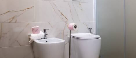 A bathroom with a marble wall, a sink, a toilet, and a roll of toilet paper on a holder.