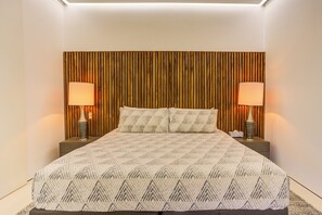 Un dormitorio moderno con una colcha de estampado geométrico, dos lámparas de noche y un cabecero de listones de madera.