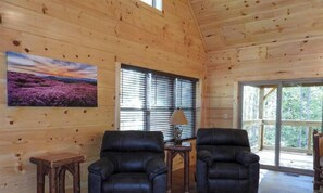 Ein Holzblockhaus-Interieur mit zwei Ledersesseln, einem kleinen Holztisch und einem Gemälde einer violetten Landschaft.