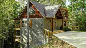 A cabin with a wooden exterior, a covered porch, and a concrete driveway.