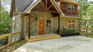 A two-story house with a stone facade, a wooden front porch, and a small deck.