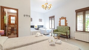 Ein Hotelzimmer mit zwei Betten, einem grünen Sessel, einem Spiegel und einer Kandelaber.