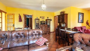 Ein Wohnzimmer mit braunem Ledersofa, einem Holzesstisch und Stühlen. Es gibt eine Küchenzeile mit Schränken und einem Kühlschrank.