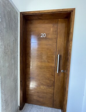 Eine Holztür mit der Nummer 20, einem Metallgriff und einer angrenzenden Betonwand.