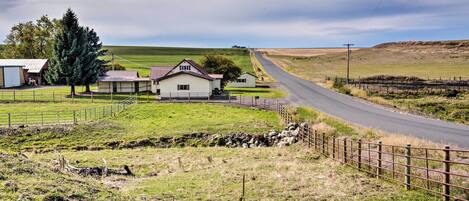 A rural road with a white house and a fenced area.