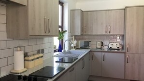 Une cuisine moderne avec des meubles en bois clair, un plan de travail noir et des appareils en acier inoxydable, notamment un four à micro-ondes et un grille-pain.