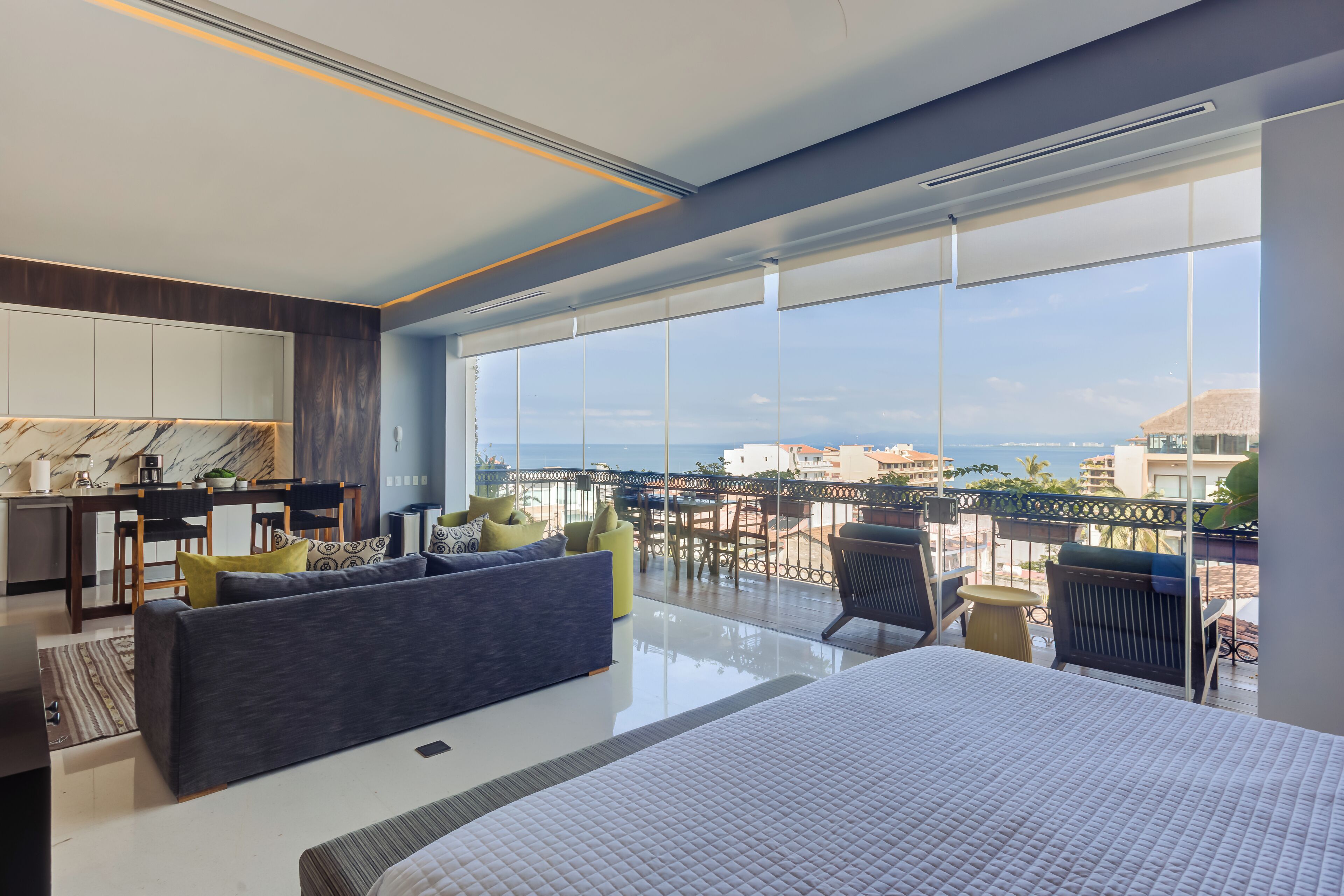 Une chambre d’hôtel moderne dotée d’un grand lit, d’un canapé, d’un coin repas et d’un balcon offrant une vue sur la ville et la mer.