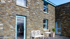 A stone building with a blue door and windows, a white bench, a small table, and a potted plant.