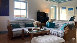 A cozy room with a sofa, a small table, and a bed. There are windows, a fireplace, and framed pictures on the wall.
