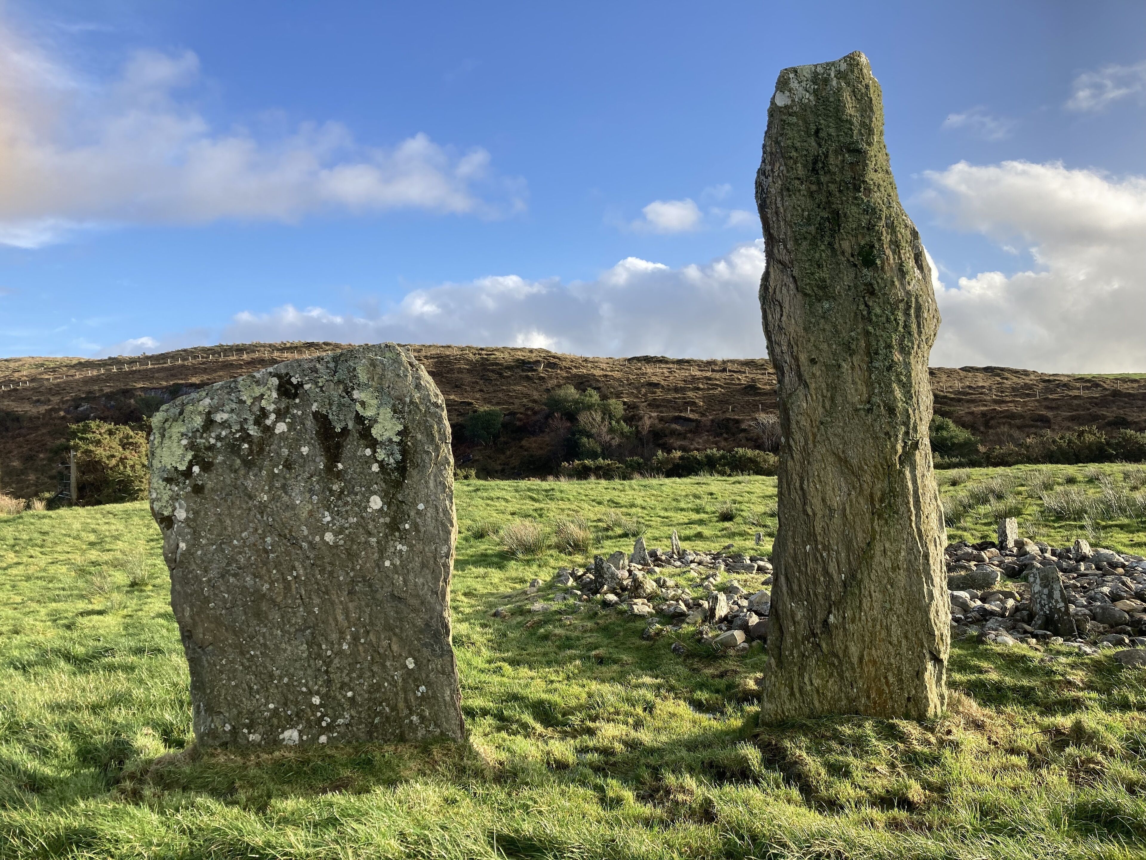 Two standing stones in a grassy field with a hilly landscape in the background.