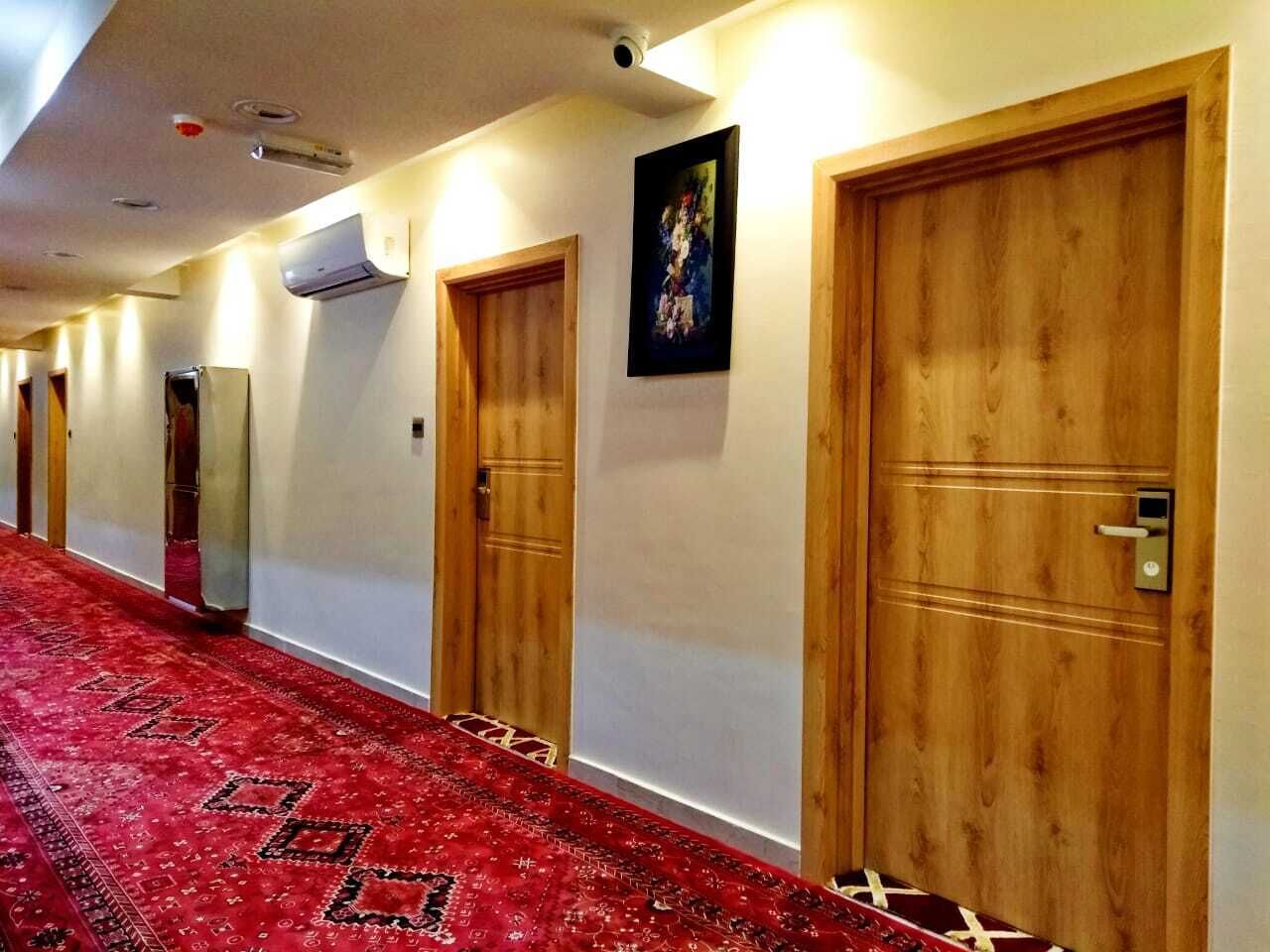 A hallway with wooden doors, a red carpet, and an air conditioning unit on the wall.