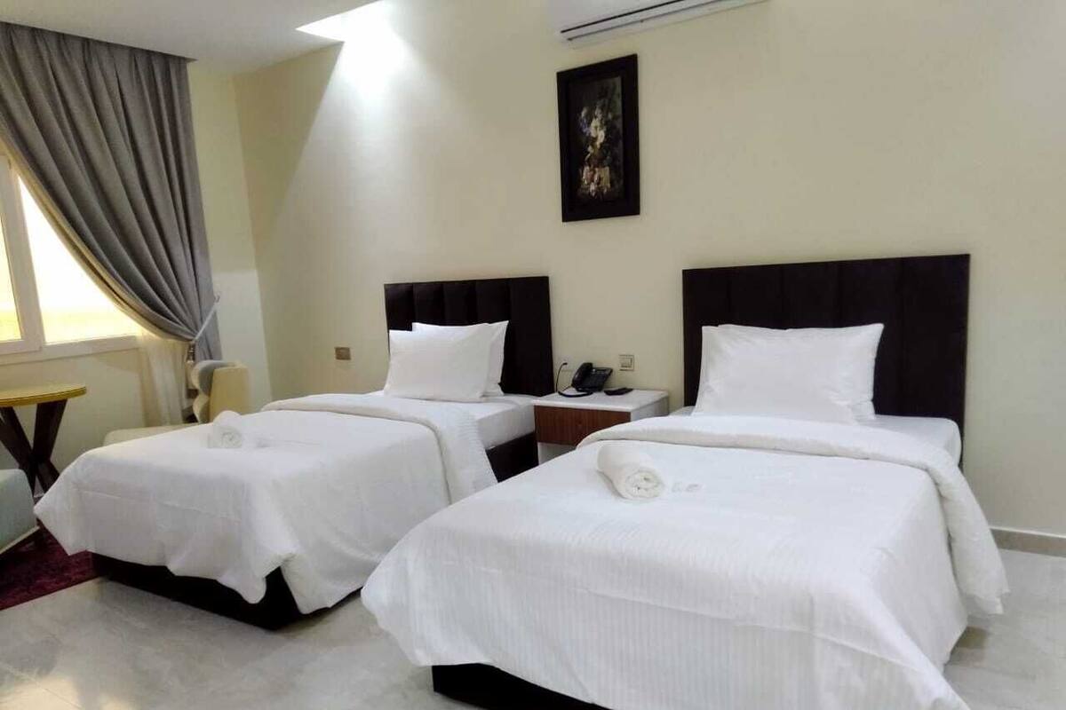 Habitación de hotel con dos camas, una mesita y un cuadro en la pared.