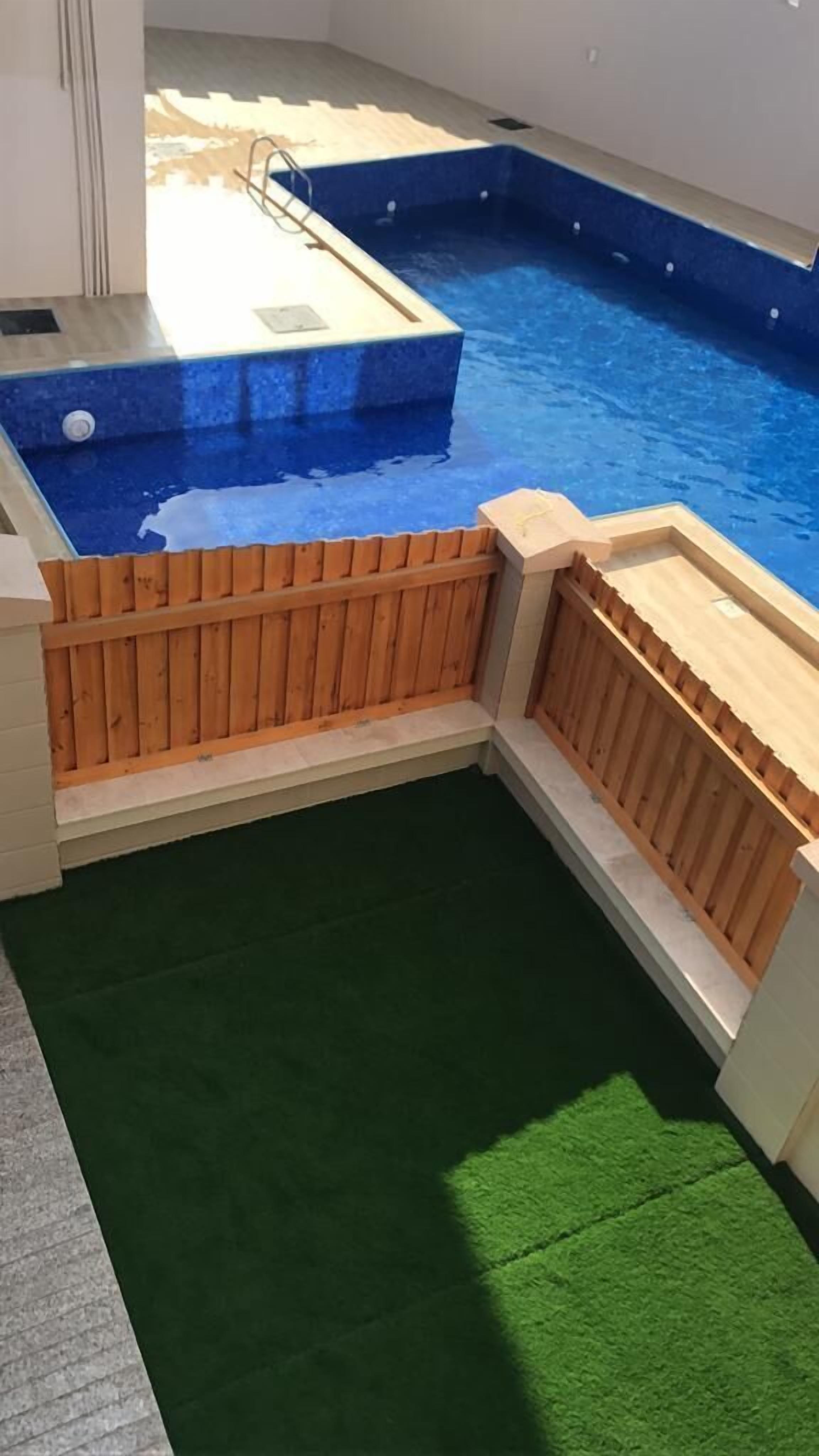 A swimming pool with a wooden deck and a green artificial turf area.