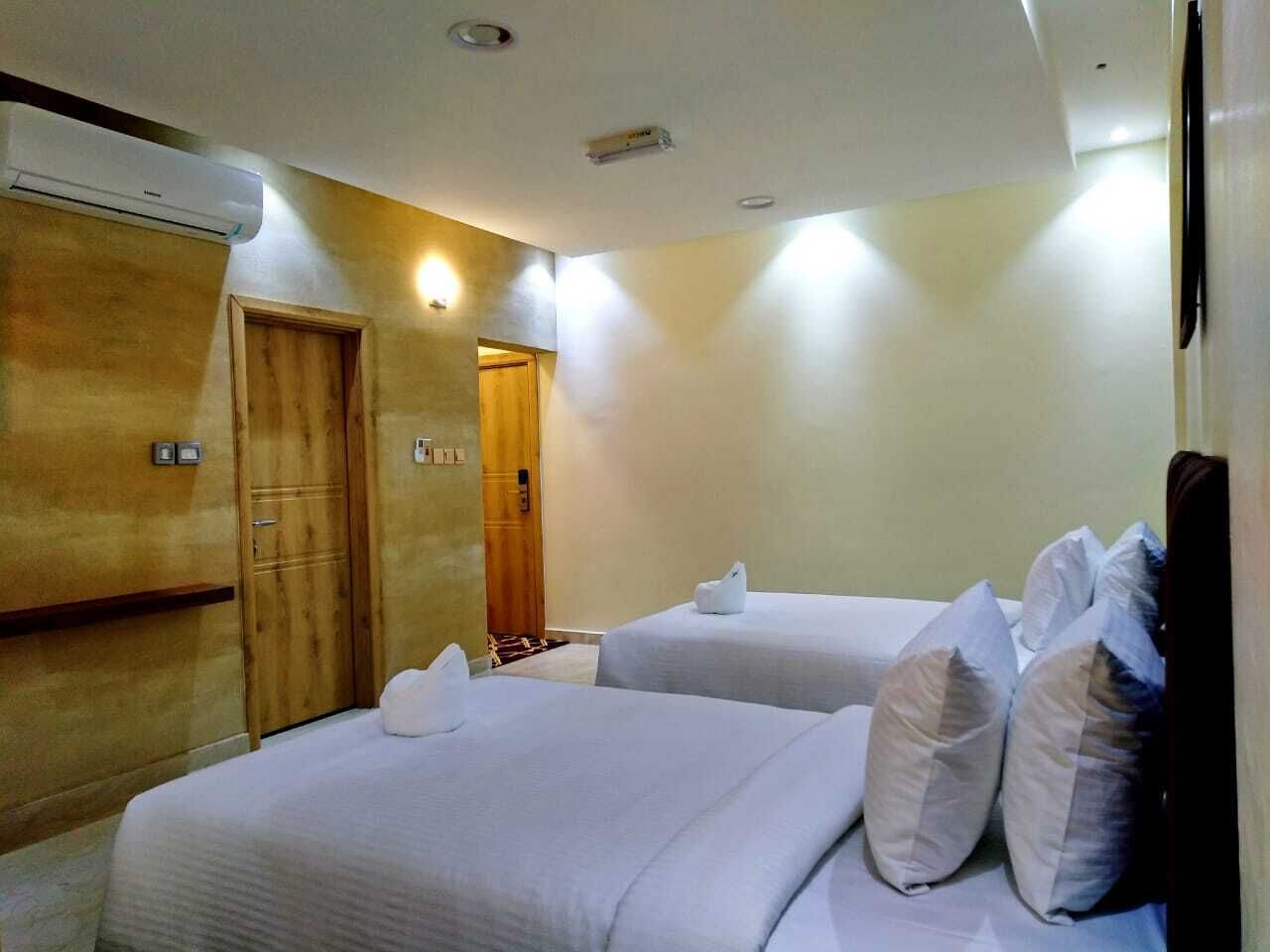 A hotel room with two beds, wooden wardrobe, and an air conditioning unit.
