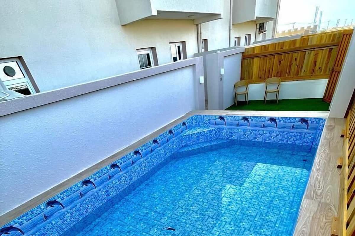 Una piscina en la azotea con suelo de baldosas y terraza de madera alrededor.