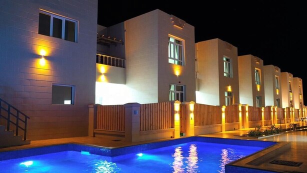 A modern hotel with a swimming pool, illuminated exterior, and a series of balconies. - Al Asala Resort (Al Hadd)