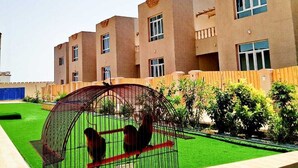 A building with multiple floors, a courtyard with green grass, and a birdcage with two birds. - Al Asala Resort (Al Hadd)