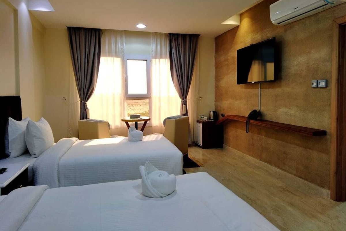 Una habitación de hotel con dos camas, un televisor montado en la pared y una pequeña mesa con una silla.