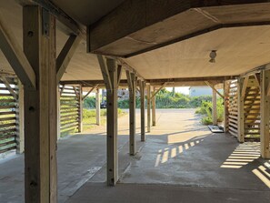 A covered outdoor area with wooden beams and a concrete floor, leading to a parking lot. - Sunrise to Sunset - Steps From the Ocean! Hot Tub! (Kitty Hawk)